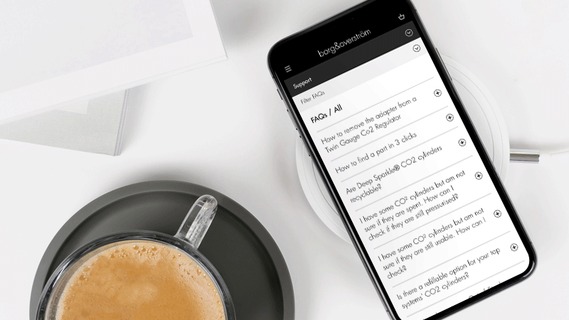 A mobile phone, positioned besides a mug of coffee, displaying the Borg & Overström FAQ support page,.