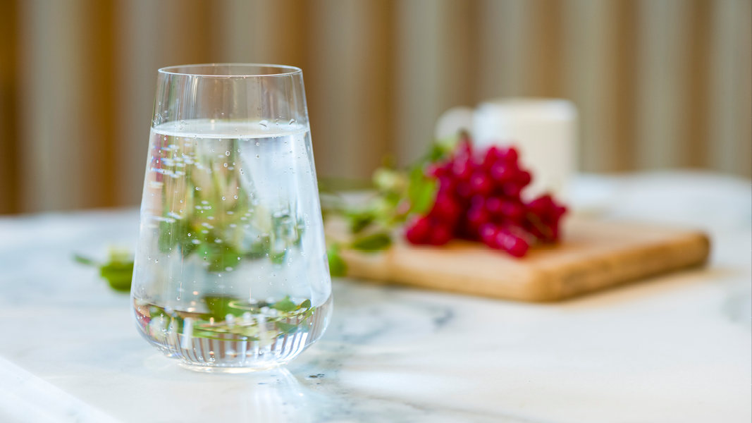 Glass of chilled water with added mint positioned next to a wooden slate with fresh red grapes on top.