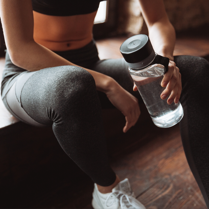 A woman resting after a workout, hydrating with a clear water bottle that she is holding.
