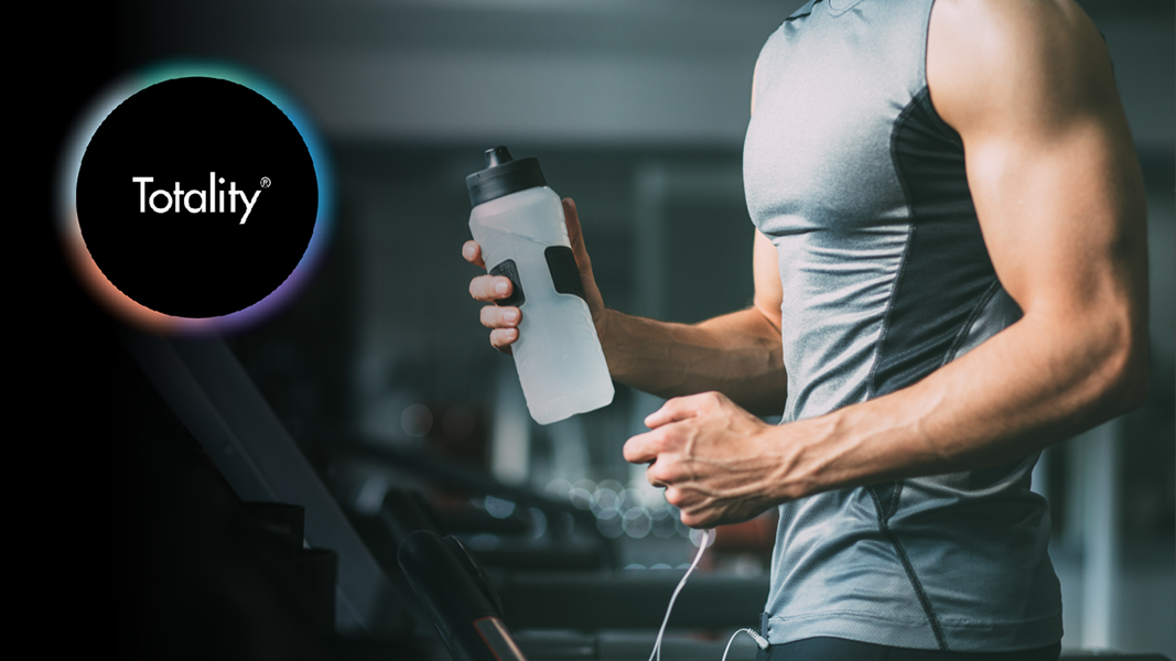 A Totality Logo faintly appearing beside a male athlete running on a treadmill, holding a water bottle