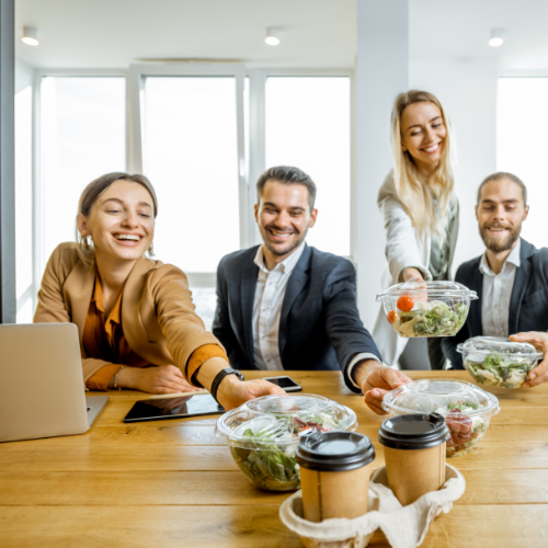 Office workspace with a group of male and female employees reaching for a healthy salad located in the middle of a worktop
