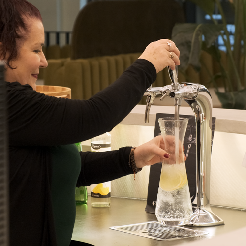 A women using a Borg & Overström C2 tap, dispensing sparkling water into a tall vessel with lemon.