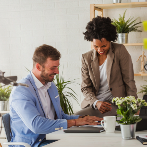 A male and female colleague discussing work in a bright office surrounded by green plantlife. 