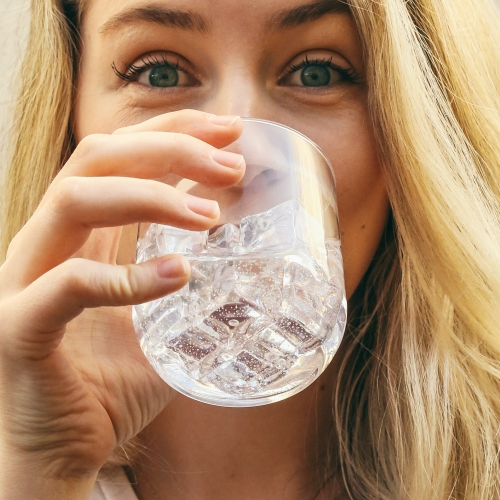 A close-up picture of a happy blonde female drinking a glass of chilled water and ice.