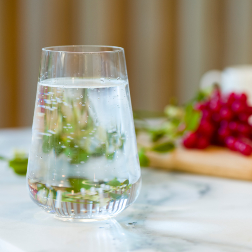 Focused image of a glass of water on top of a marble kitchen worktop with a variety of berries blurred in the background