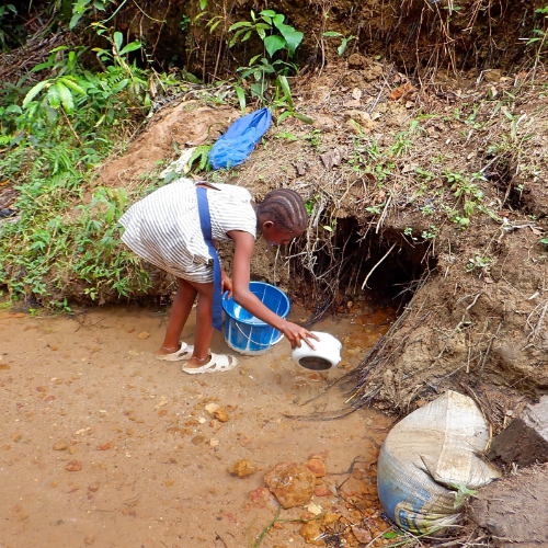 A young child collecting water from a shallow stream