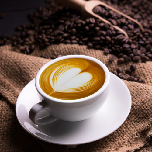 A mug of coffee with a love heart shaped using light cream, positioned next to an empty sack of roasted coffee beans.