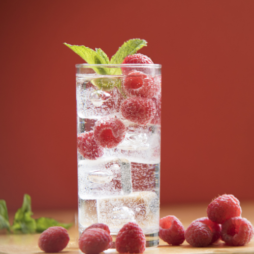 A glass of sparkling water, filled with ice, raspberries, and a single mint leaf. 