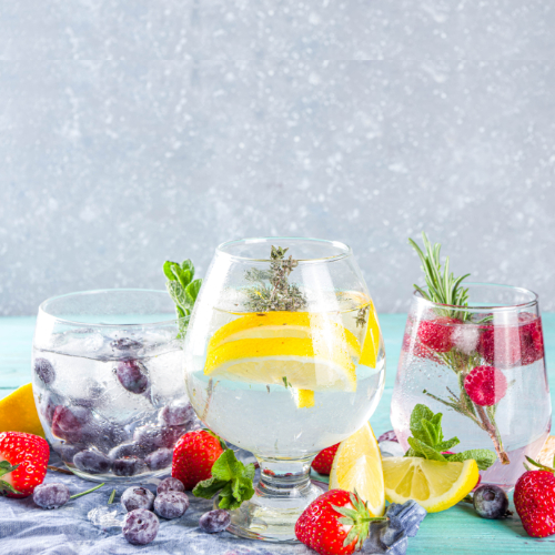 Three glasses of water aligned next to each other, all filled with a different fruity infusion: blackberries, lemon, and raspberry.