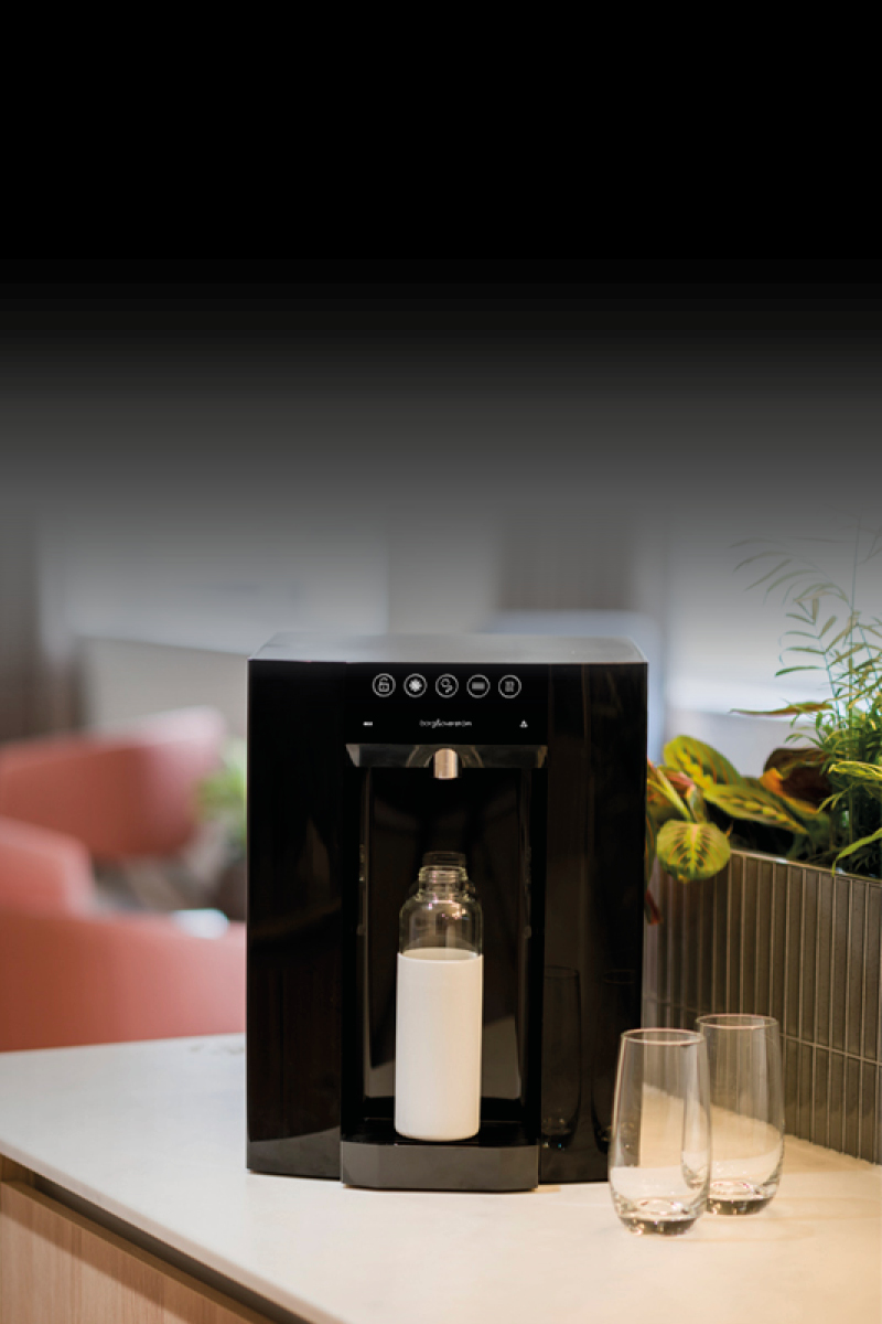 A Borg & Overström E6 countertop, in focus, with 2 glasses sitting by the right-side and a water bottle positioned in the dispense space.